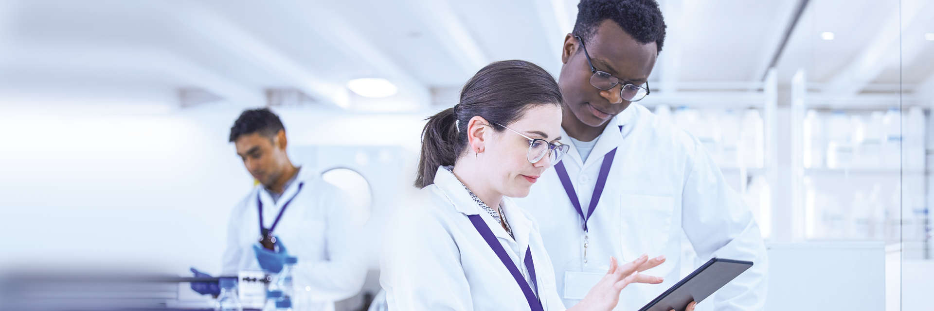 Enzymes, NGS, Caucasian female talking to black male with mobile device with a black male in background in a laboratory setting